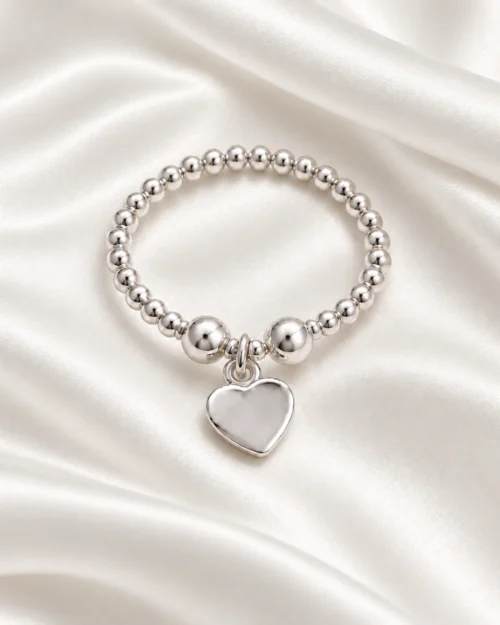 Anillo Origen de bolas de plata de ley 925 con charm de corazón colgante, sobre tela satinada color crema