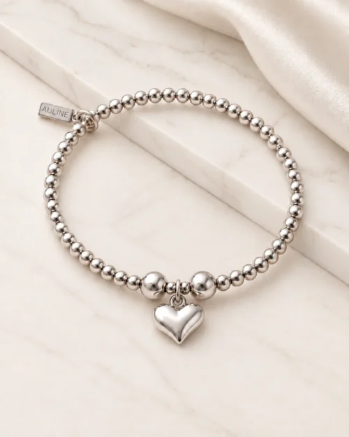 Pulsera Origen de bolas de plata de ley 925 con charm de corazón, sobre base de mármol color crema con tela satinada