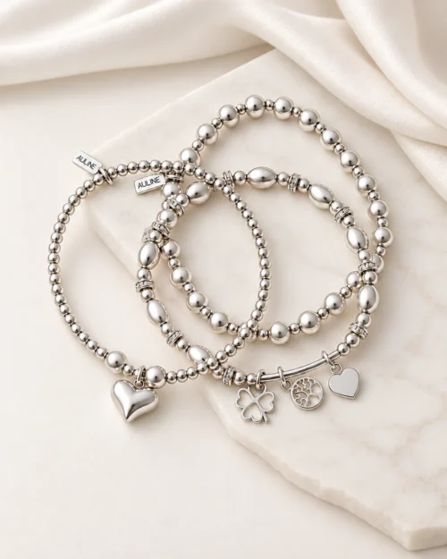 Set Trío Esencia de tres pulseras de plata de ley 925 con bolas, perlas naturales y colgantes de corazón, trébol y árbol de la vida, sobre tela color crema